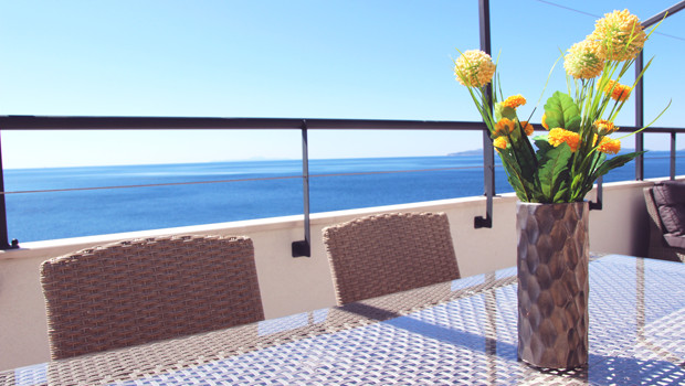 A table with flowers and a view of the sea from an apartment balcony